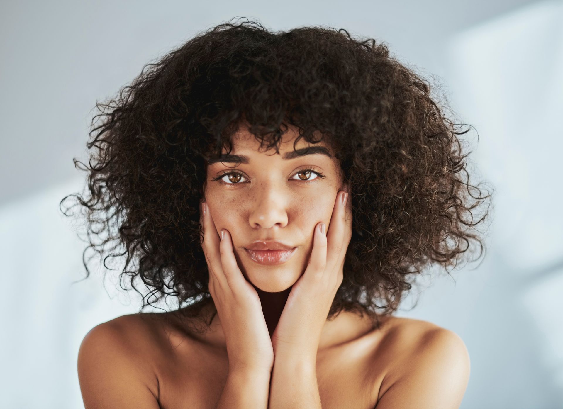 A woman with curly hair is covering her face with her hands.