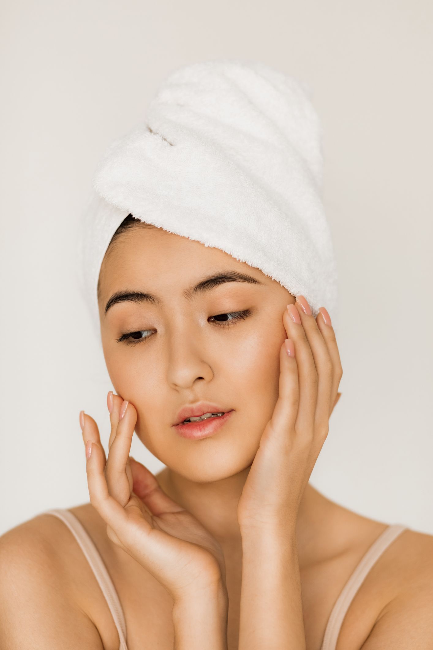 A woman with a towel wrapped around her head is looking at her face.