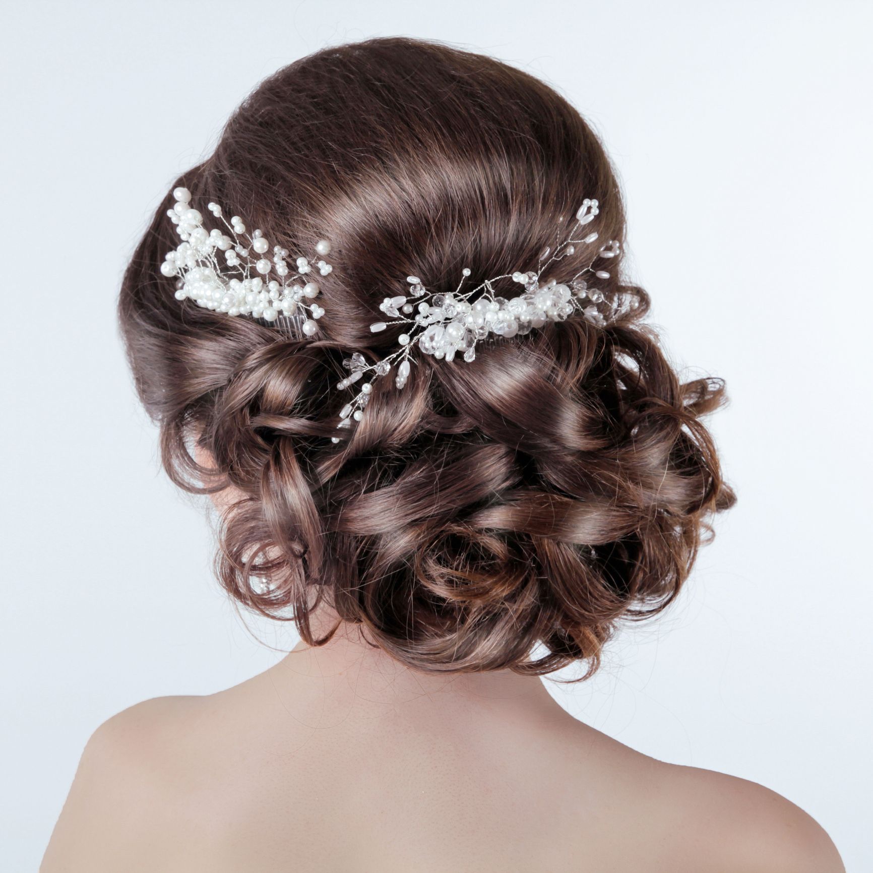 The back of a woman 's head with her hair in a bun with pearls and rhinestones.