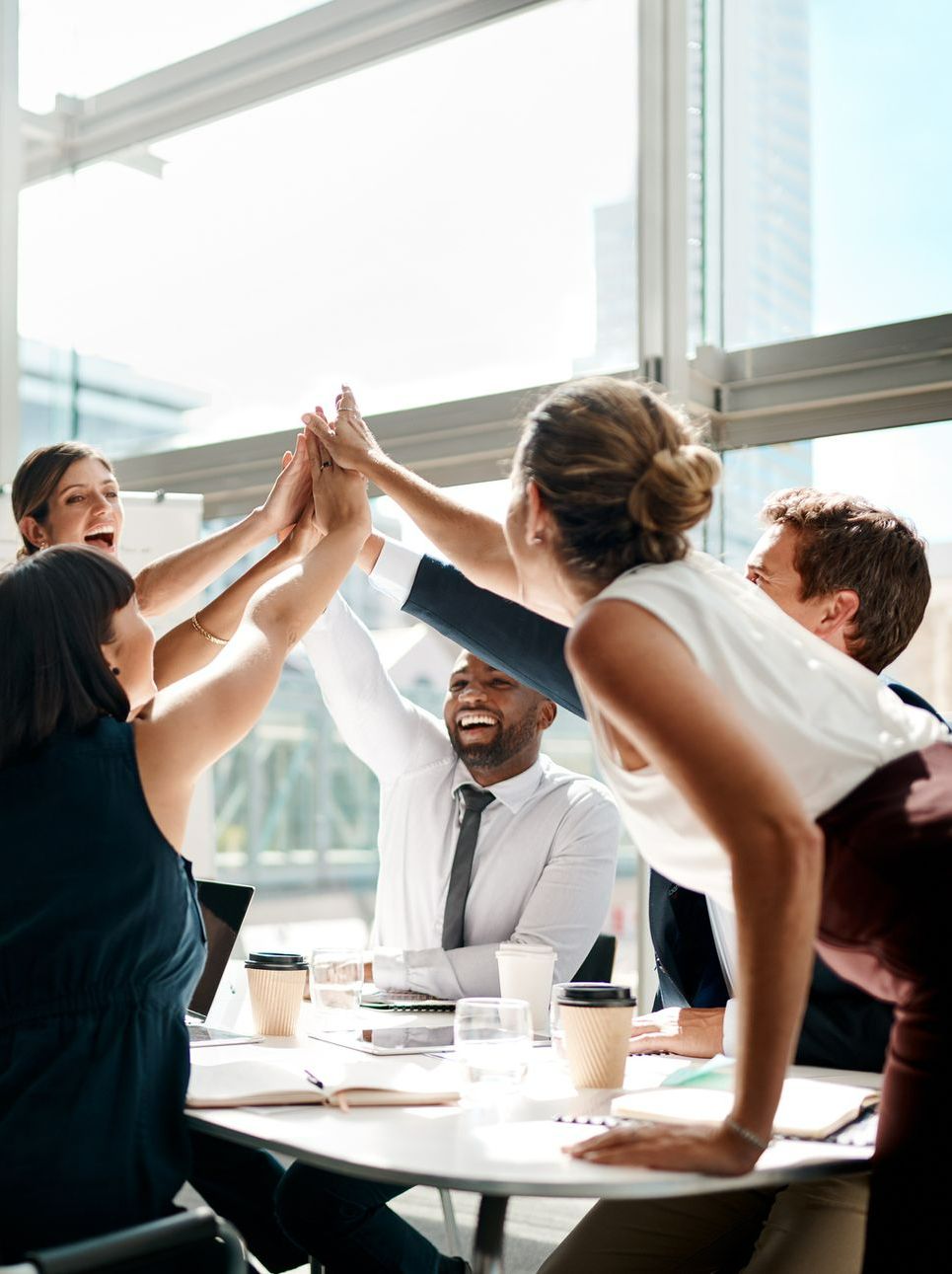A group of people are giving each other a high five while sitting around a table - The Woodlands, TX - Premiere Services