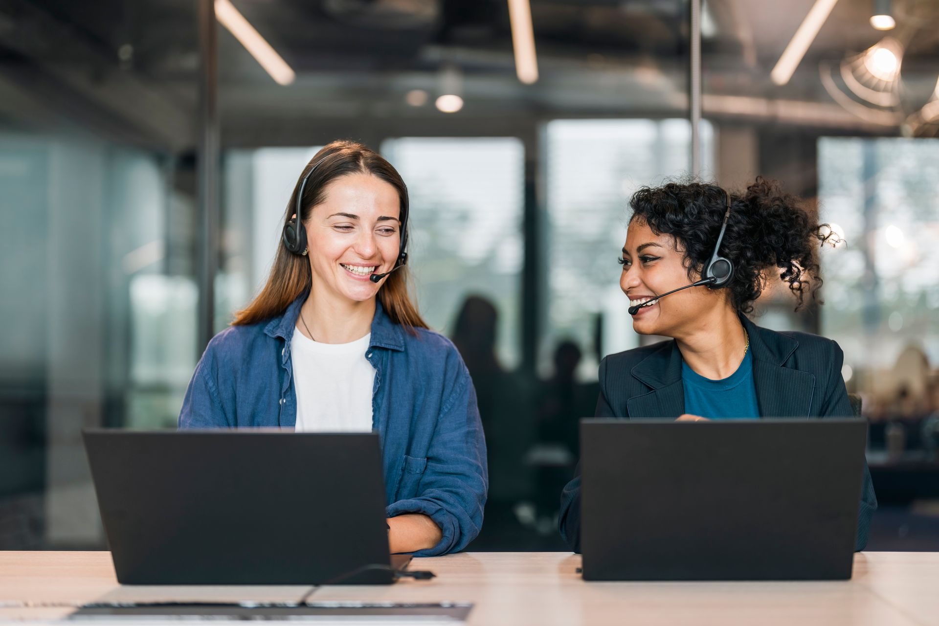 Two women wearing headsets are sitting at a desk with laptops - The Woodlands, TX - Premiere Services