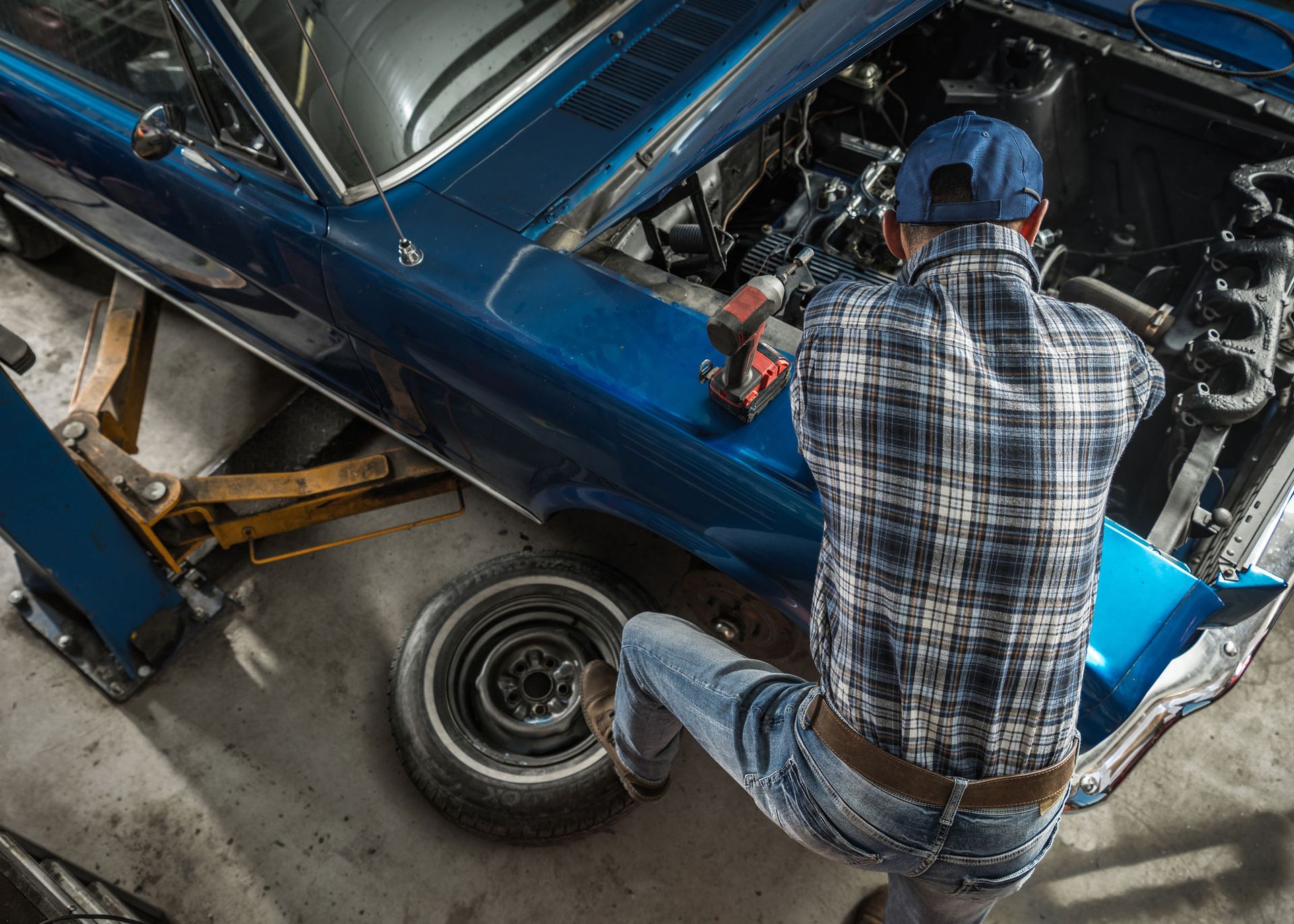 Mechanic working on a blue classic car with the hood open, in a garage setting.