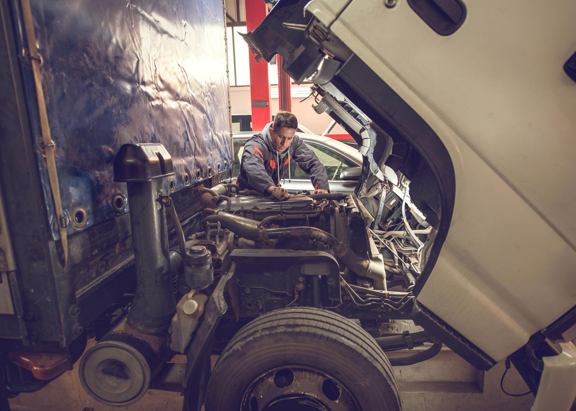 Mechanic working on a truck engine, under the hood. Inside a garage.