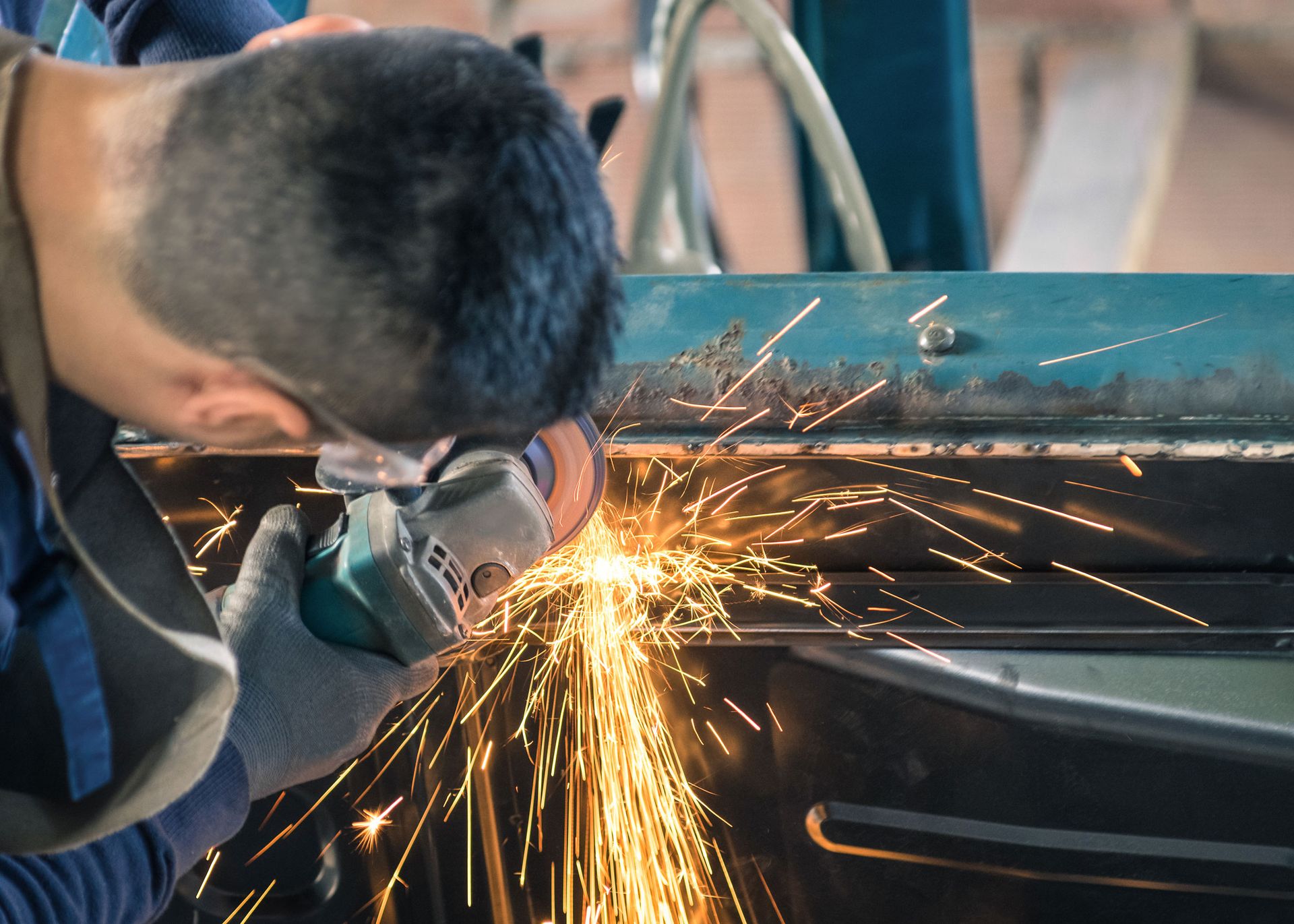 Person grinding metal, creating sparks, wearing gloves, outdoors.