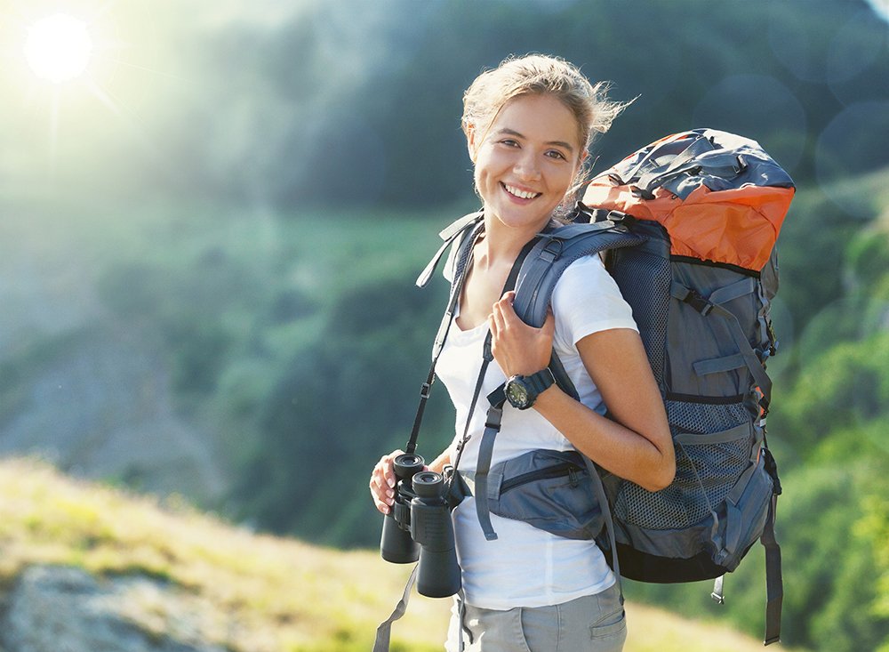 Una mujer con una mochila y binoculares está caminando por las montañas.