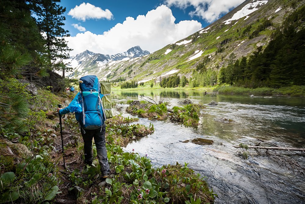 Una persona con una mochila camina a lo largo de un río en las montañas.
