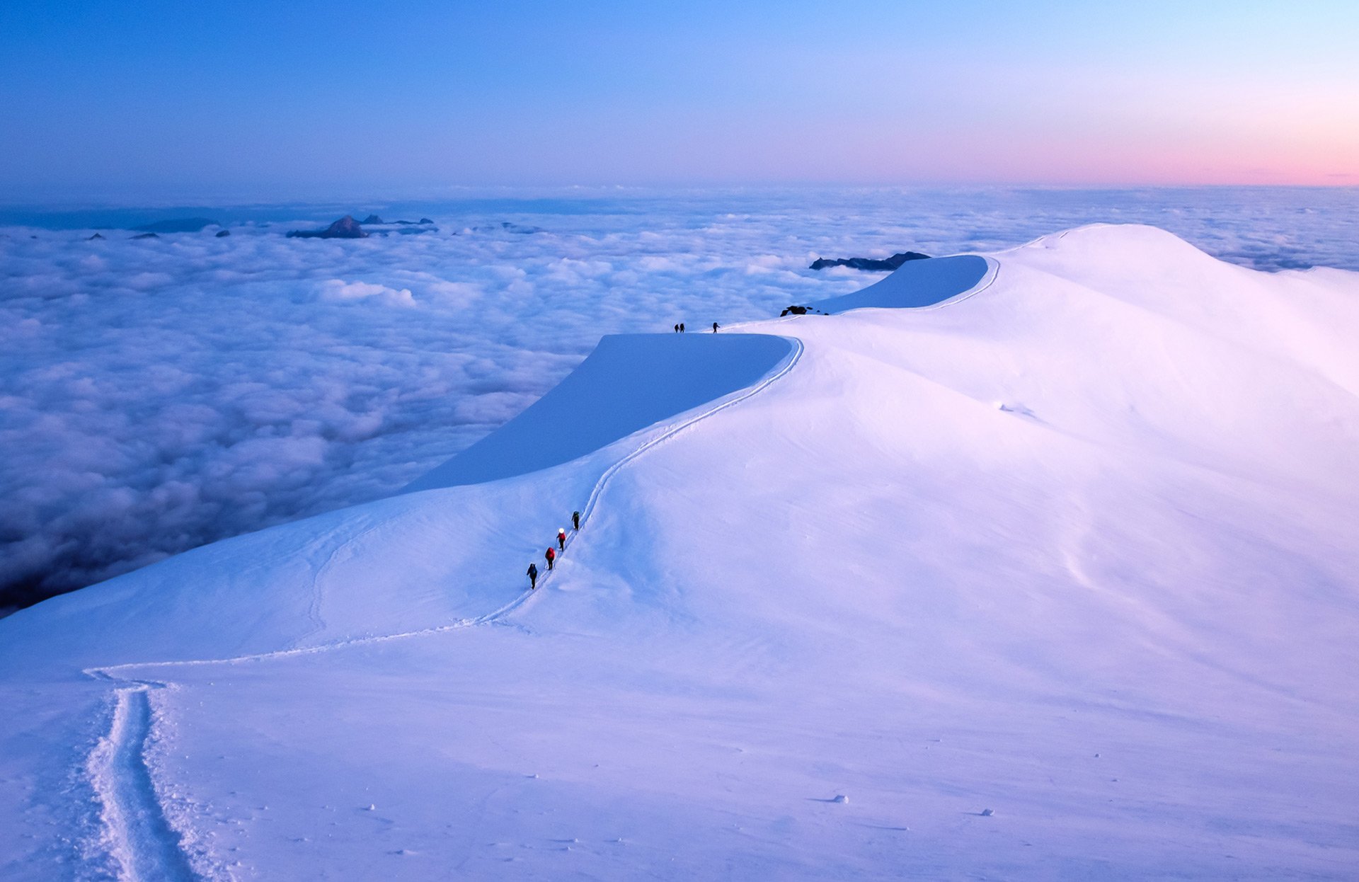 A group of people are walking up a snow covered mountain.