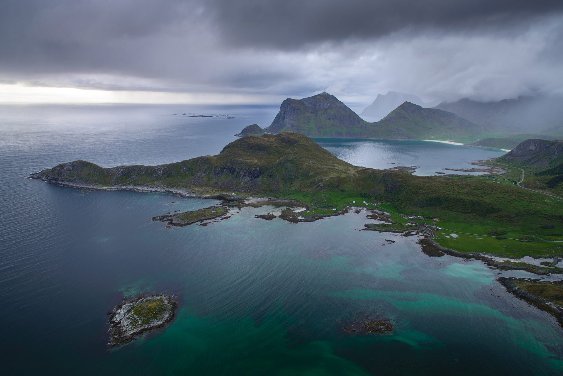 An aerial view of a small island in the middle of the ocean with mountains in the background.