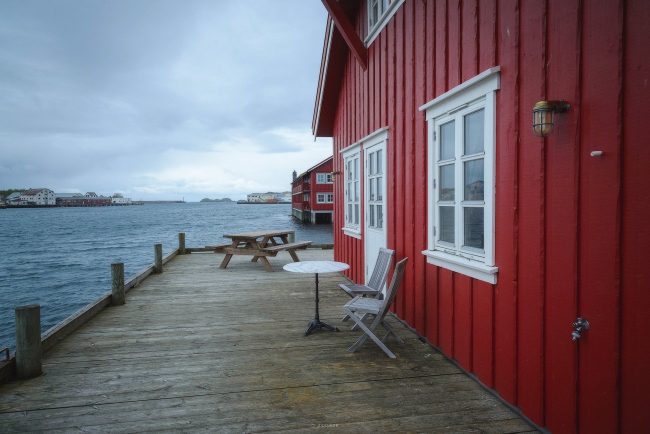 A red house with a table and chairs on the dock next to the water.
