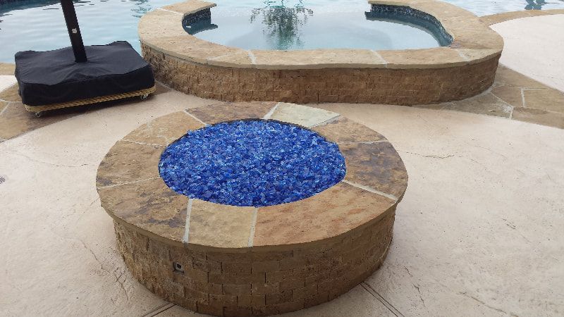 A fire pit surrounded by blue glass next to a pool.