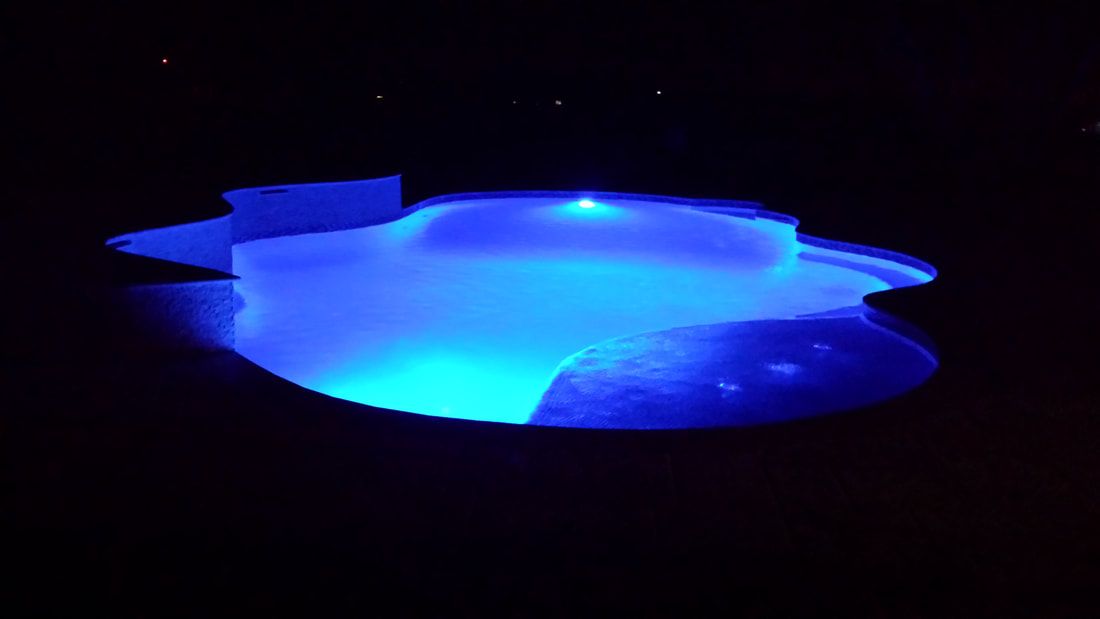 A swimming pool is lit up with blue lights at night.