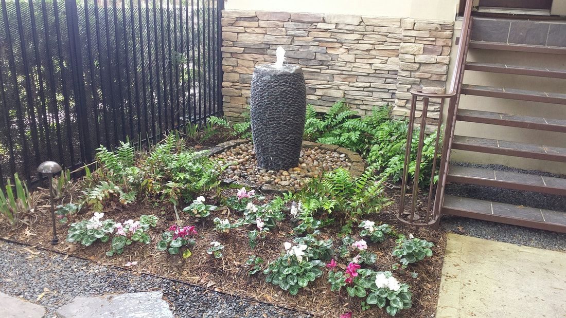 There is a fountain in the middle of a garden next to stairs.