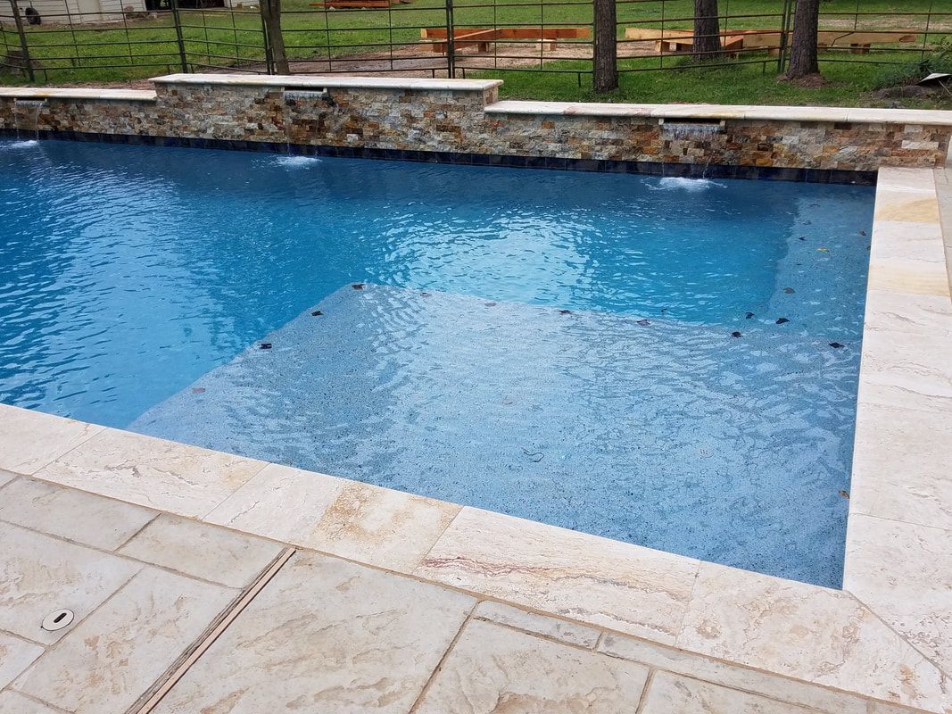 A large swimming pool surrounded by a stone wall and a patio.