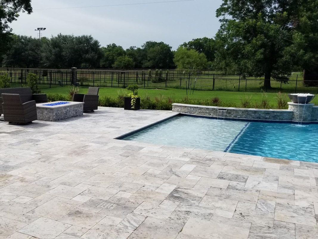 A large swimming pool is surrounded by a patio with a fire pit and chairs.