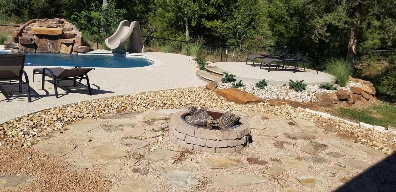 A fire pit is in the middle of a patio next to a pool.