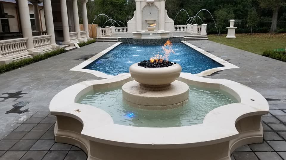 A large fountain in front of a large swimming pool.