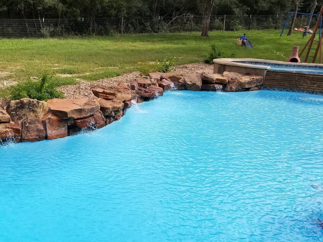 A large swimming pool surrounded by rocks and grass in a backyard.