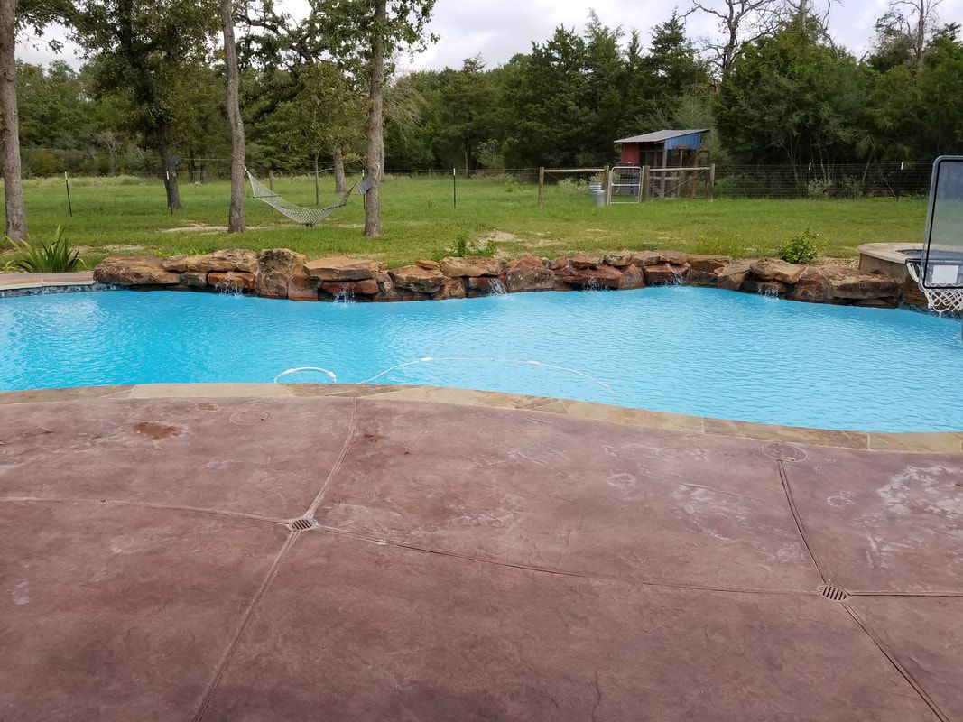 A large swimming pool surrounded by rocks and trees in a backyard.