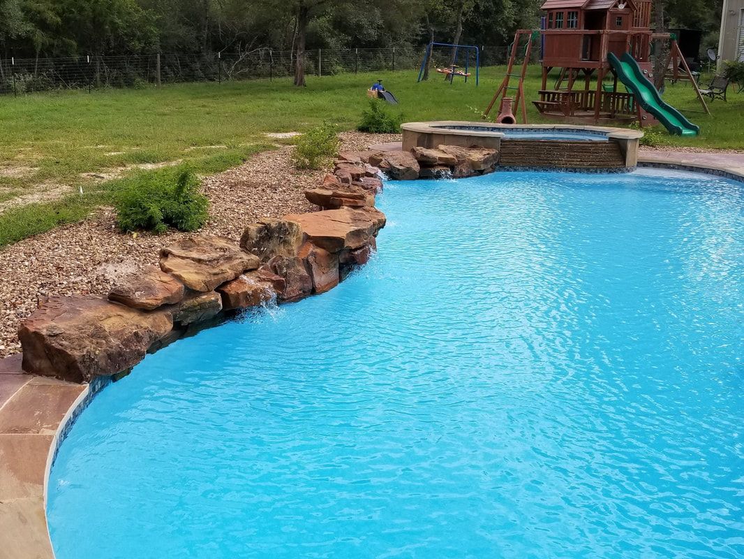 A large swimming pool with a waterfall and a playground in the background.