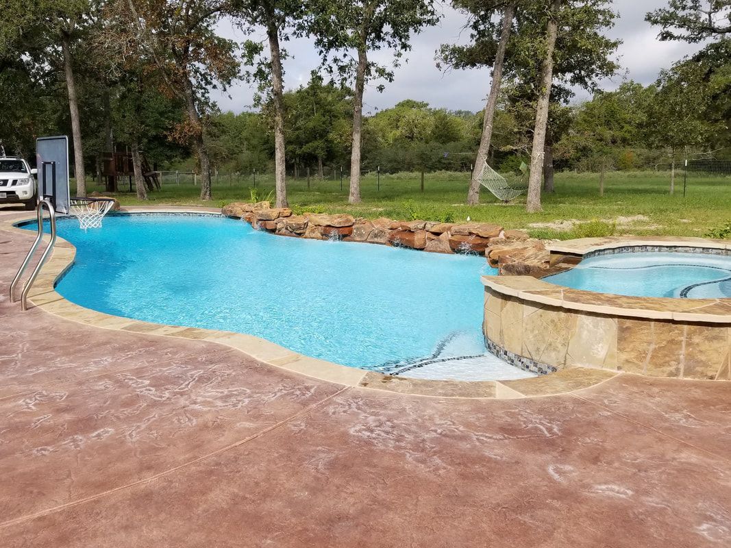 A large swimming pool with a hot tub and trees in the background.
