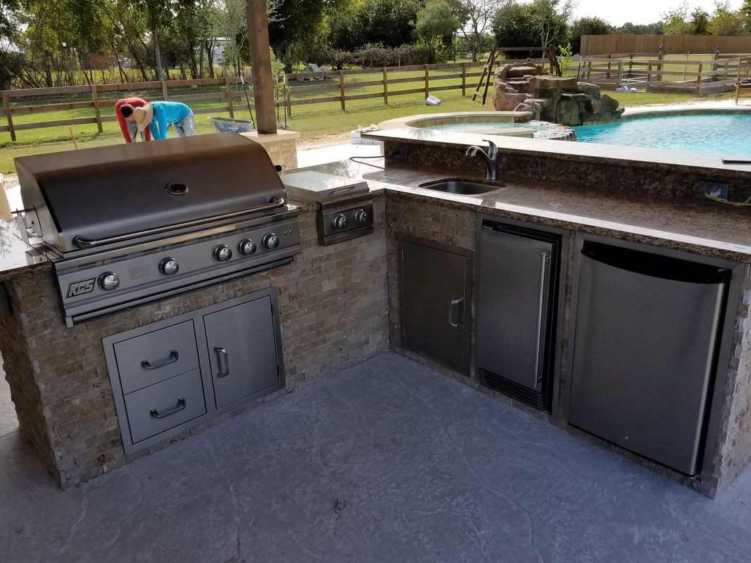 An outdoor kitchen with a grill , sink , and dishwasher next to a pool.