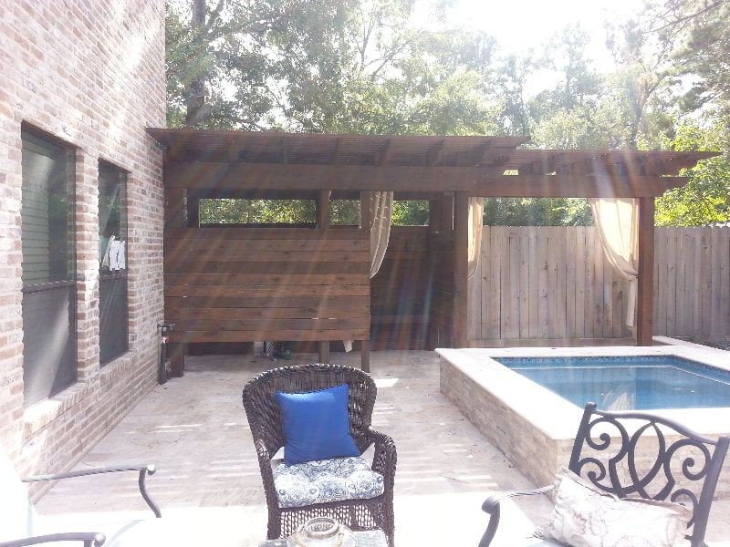 A patio with a chair and a blue pillow next to a pool.