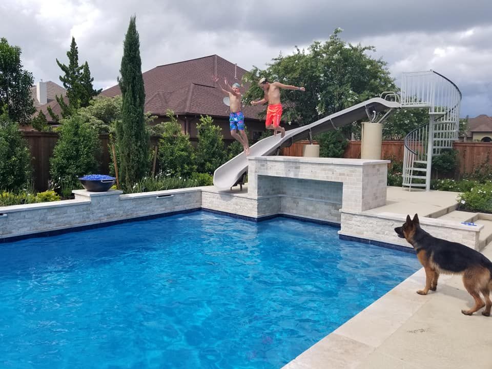A man is jumping off a slide into a pool while a dog watches