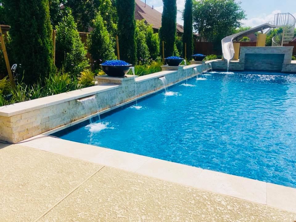 A large swimming pool with a waterfall and a slide in the background.