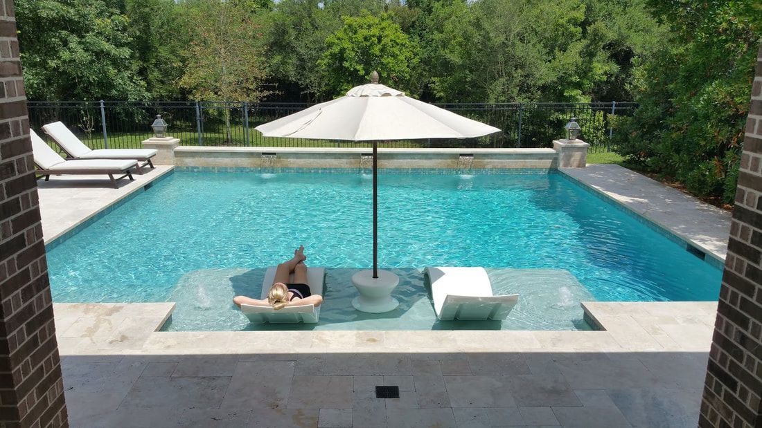 A woman is laying on a chair in a swimming pool under an umbrella.