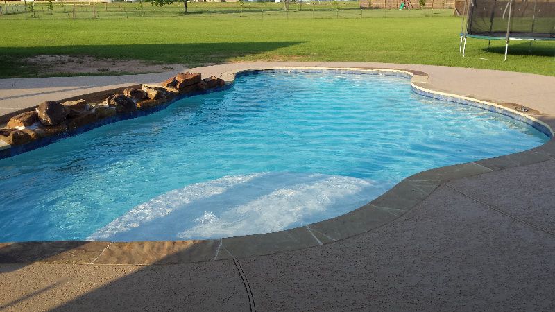A large swimming pool with a trampoline in the background.