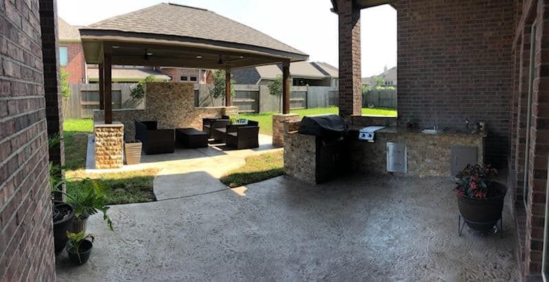 A patio with a gazebo and a grill in the backyard of a house.