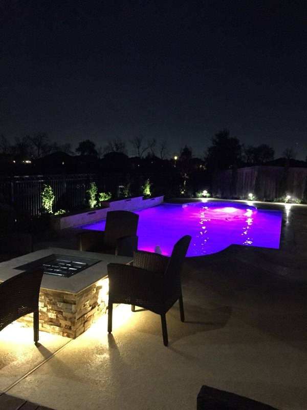 A swimming pool is lit up at night with purple lights