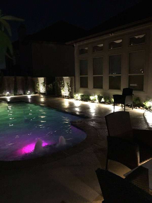 A swimming pool is lit up at night and has a fountain in it.
