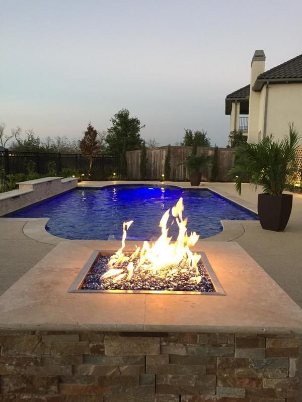 A fire pit in front of a large swimming pool