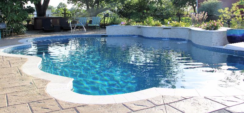 A large swimming pool is surrounded by a patio and trees