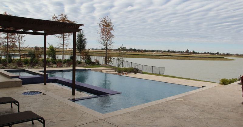 A large swimming pool with a pergola overlooking a lake.