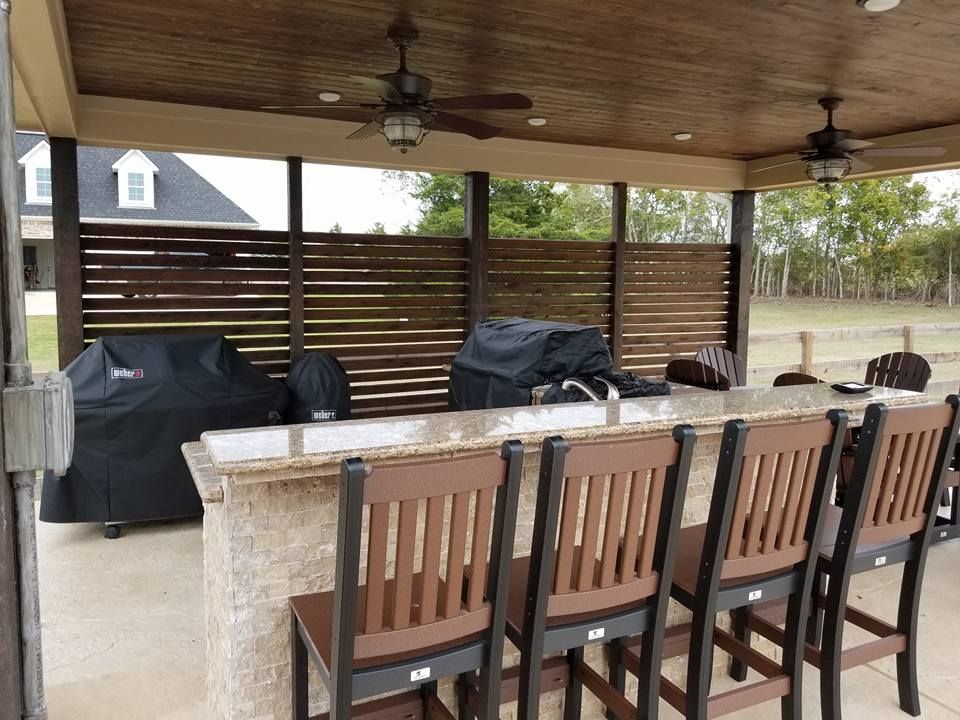 A patio with a bar , chairs , a grill and a ceiling fan.