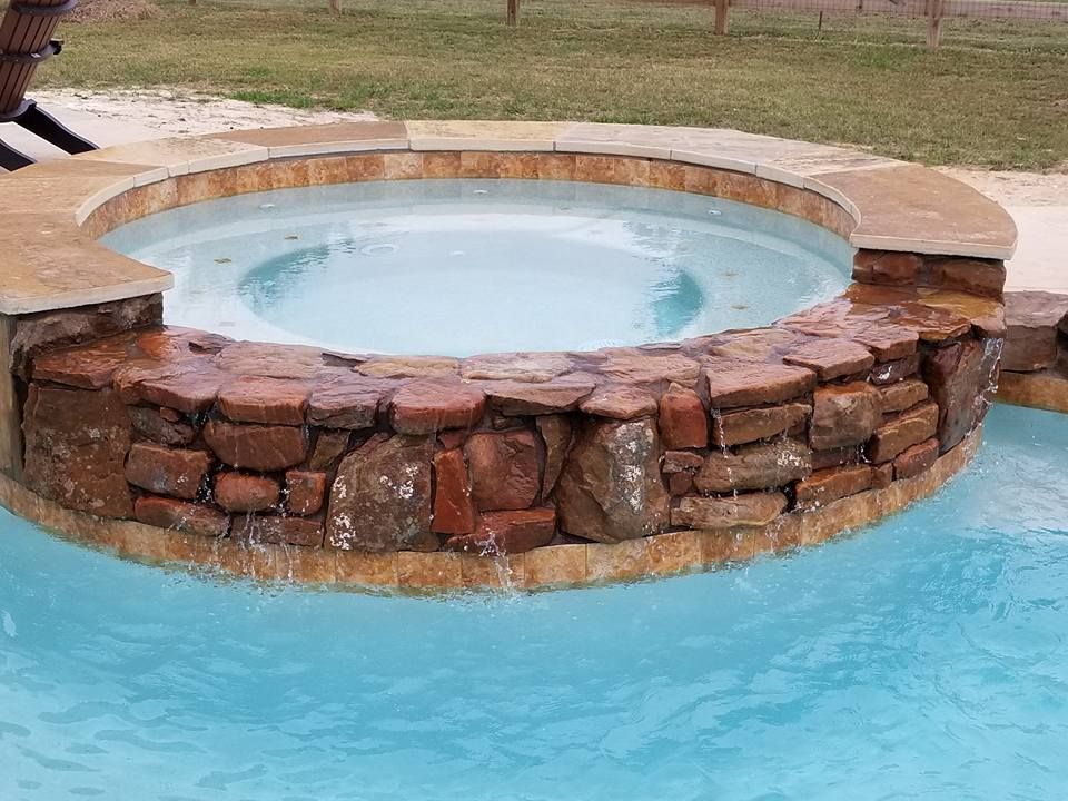 A hot tub in the middle of a swimming pool surrounded by rocks.