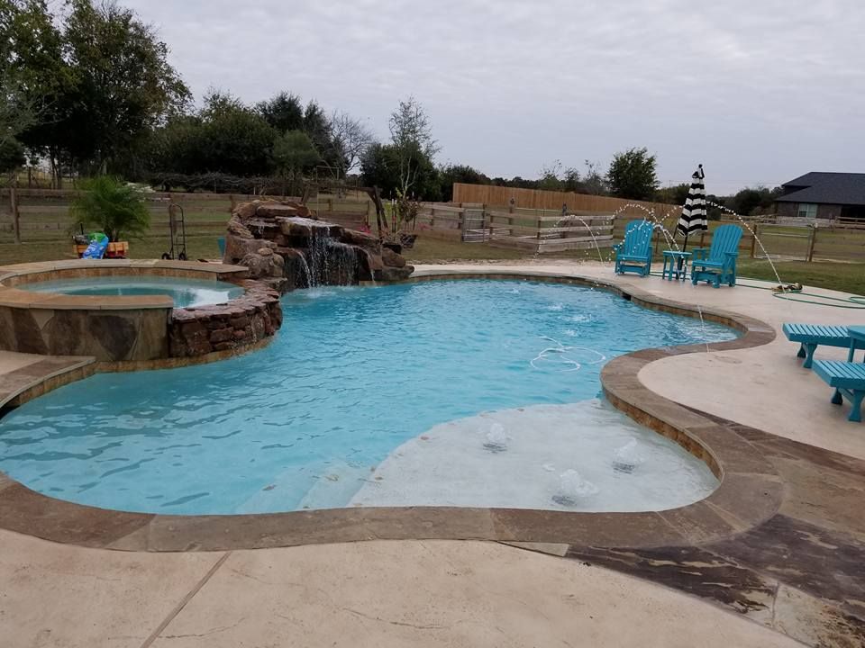 A large swimming pool with a waterfall and chairs around it.