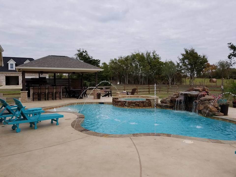 A large swimming pool with a waterfall and a gazebo in the background.