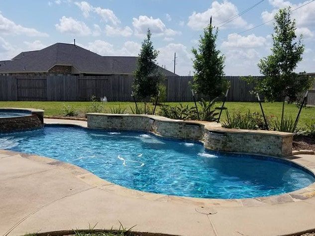 A large swimming pool with a waterfall in the backyard of a house.