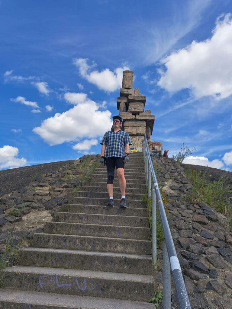 Mann steht auf der Treppe einer Halde unter blauem Himmel mit einem Steindenkmal.