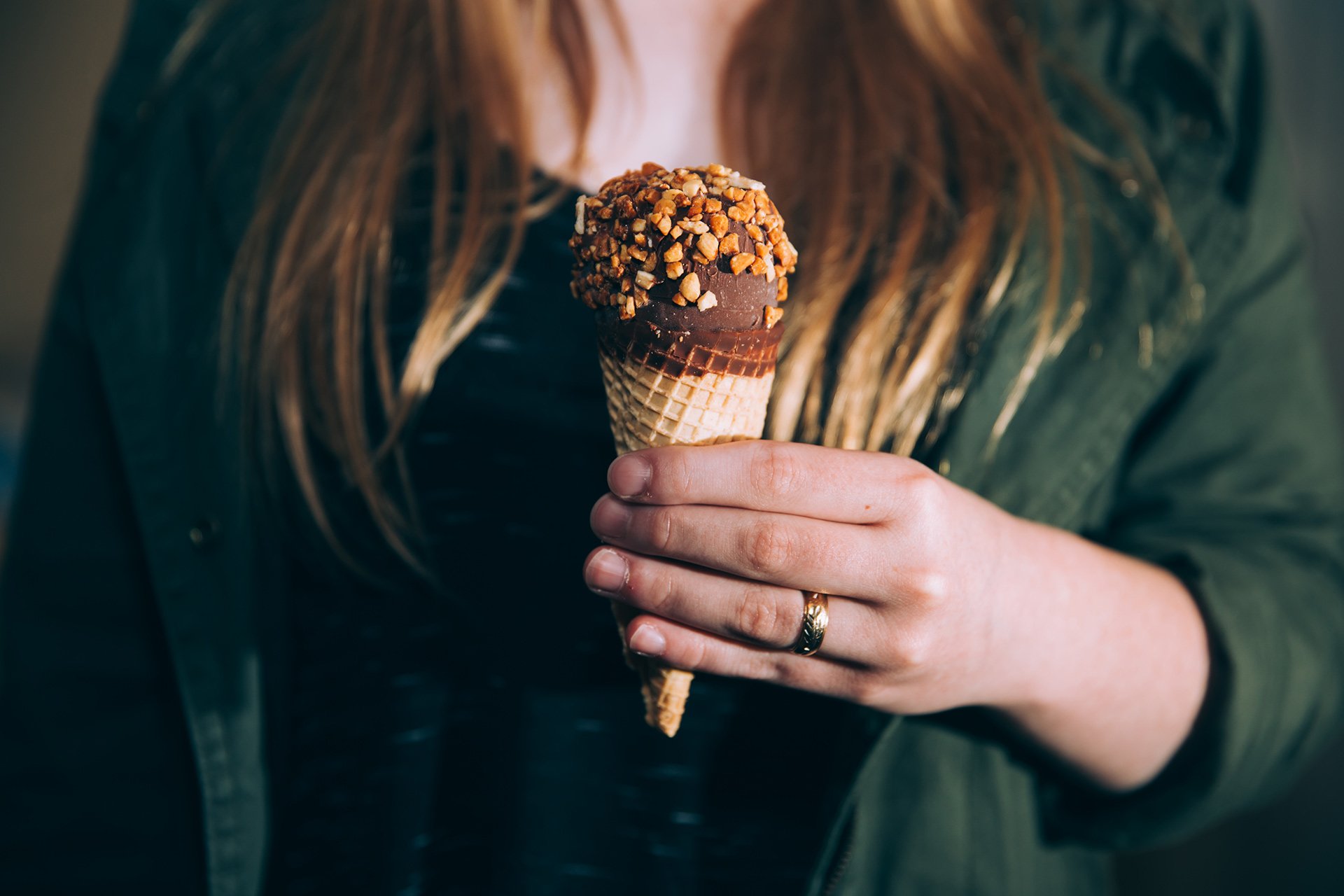 A person holds a chocolate-dipped ice cream cone topped with crushed nuts.