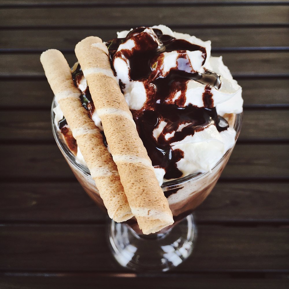 A glass of chocolate milkshake topped with whipped cream, chocolate syrup drizzle, and two crunchy wafer sticks.
