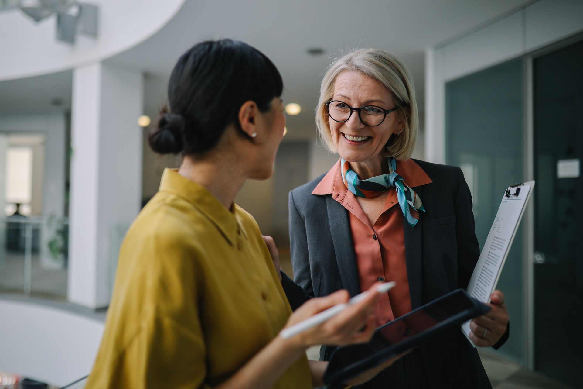 A woman is holding a clipboard and talking to another woman.