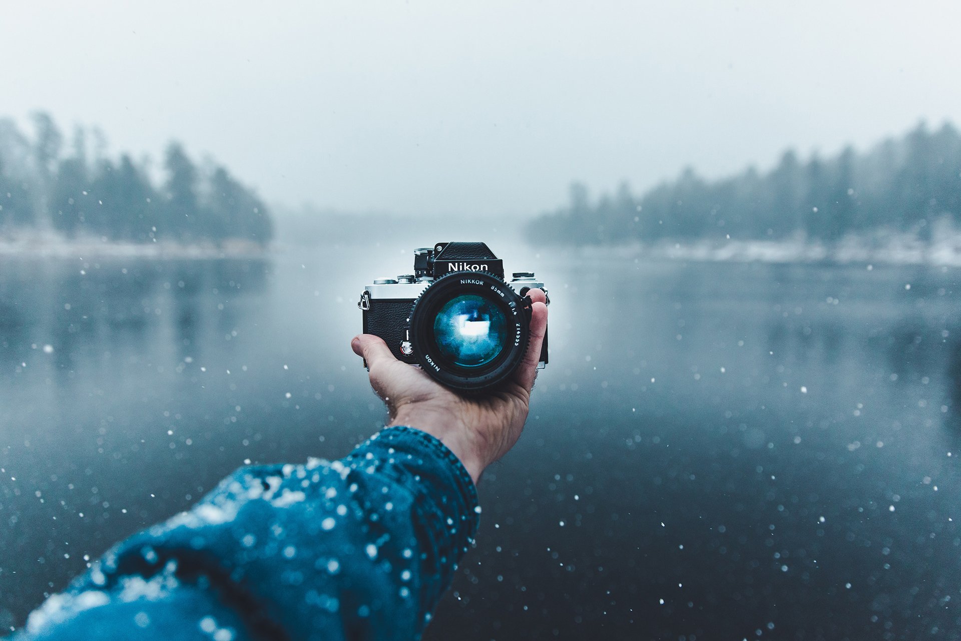 Person holding Nikon camera with scenic winter lake backdrop, capturing properties by Authority PM