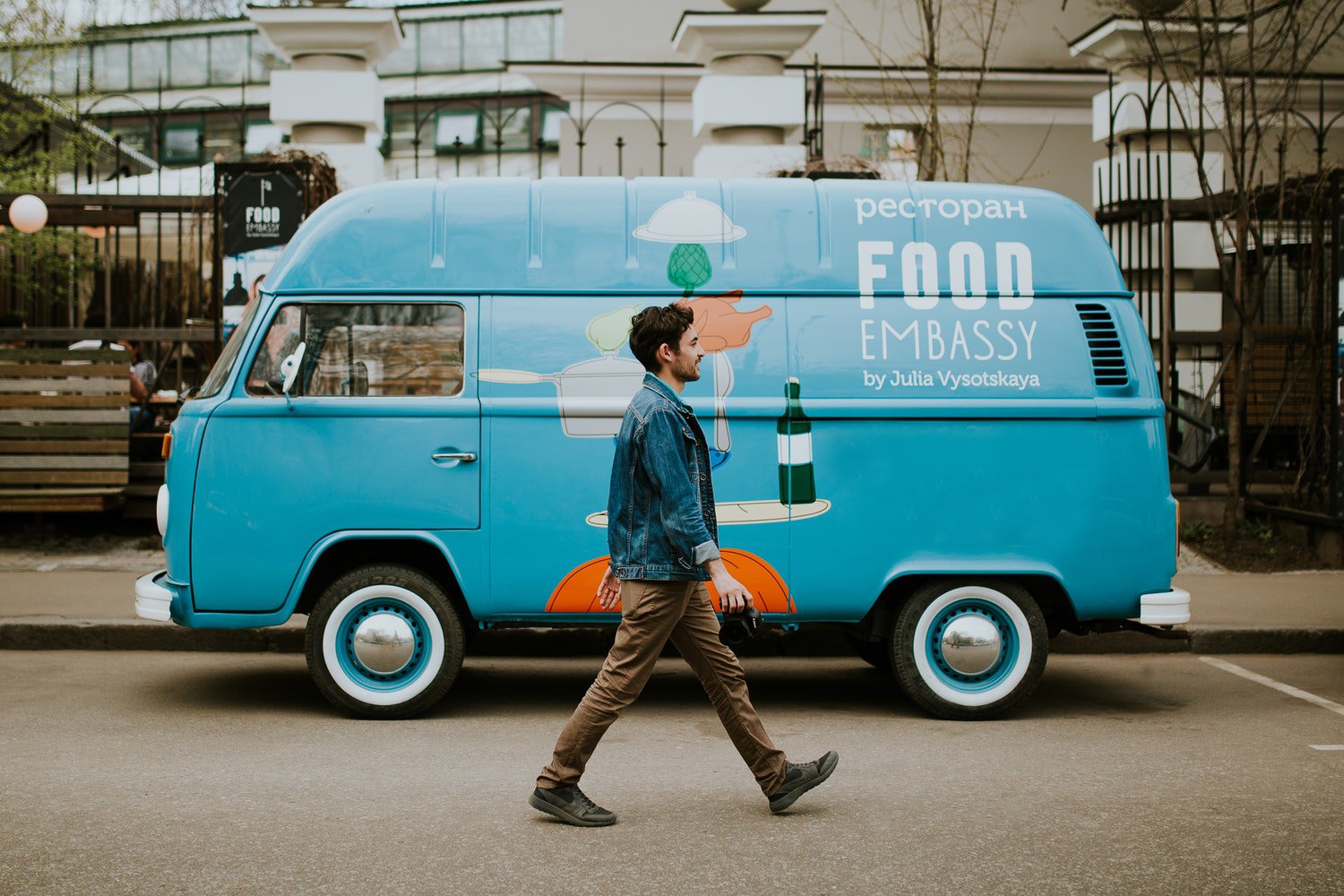 A man is walking past a blue food truck on the side of the road.