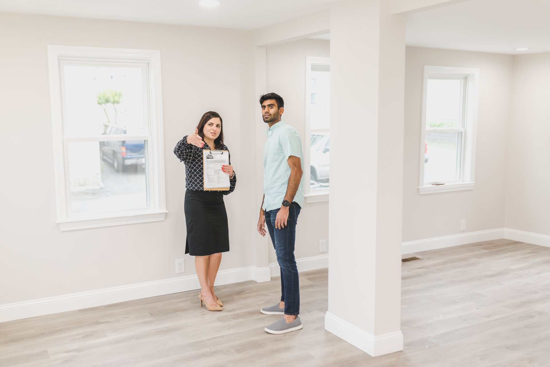 A man and a woman are standing in an empty room in a house.