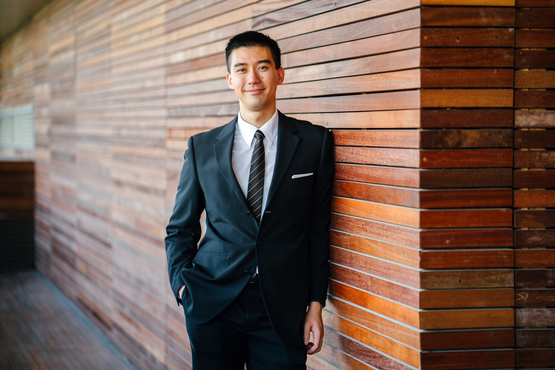 A man in a suit and tie is leaning against a wooden wall.