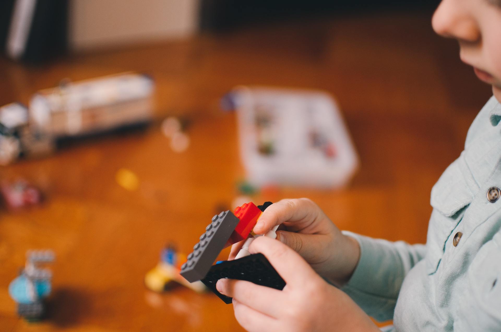A child is playing with lego blocks on a wooden table.